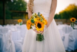 A person in a white dress holding a bouquet of sunflowers flowers